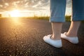 Woman in white sneakers standing on asphalt road towards sun. Travel, freedom concepts. Royalty Free Stock Photo