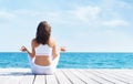 Woman in white sporty clothes meditating on a wooden pier on summer. Sea and sky background. Yoga, sport, vacation Royalty Free Stock Photo