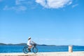 Woman riding a bicycle along stony sidewalk on blue sparkling sea water Royalty Free Stock Photo