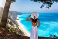 A woman in a white summer dress enjoys the view to the blue sea of Egremni Beac