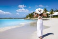 A woman in a white summer dress walks barefoot down a tropical paradise beach Royalty Free Stock Photo