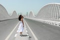 A woman in a white sundress walking on an empty road toward to the city, Meydan bridge in Dubai