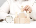 A woman in a white sweater puts a wooden figurine on the podium. The concept of employee search, career advancement. Talented