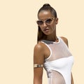 Woman in white swimsuit and golden sunglasses with hair up poses on isolated background. High fashion shot.