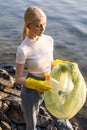 A woman in a white T-shirt and blue jeans holds a trash bag with empty plastic bottles in her hands. Clearing and Royalty Free Stock Photo