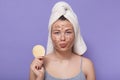 Woman with white towel on head, holding round cosmetic face sponge, being ready to removing facial mask off, peeling her face skin Royalty Free Stock Photo