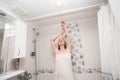 woman with a white towel, stands in the bath and stretches her arms up, relaxing in the bathroom