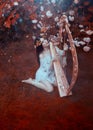 woman in a white vintage dress sits on a forest lawn and plays the golden harp