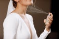 A woman in a white wedding dress gown with a neckline holds a bottle with perfume and splashes on her neck. Morning of the bride Royalty Free Stock Photo