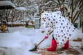 Woman in a white winter jacket and red shoes. Clears the road from snow after heavy snowfall. The girl removes snow with a shovel Royalty Free Stock Photo