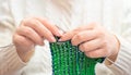 Woman in white winter warm sweater knitting a scarf with green and blue coloured yarn and knitting needles close up Royalty Free Stock Photo