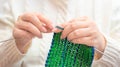 Woman in white winter warm sweater knitting a scarf with green and blue coloured yarn and knitting needles close up Royalty Free Stock Photo