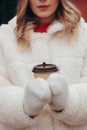 Woman in white wool mittens and fur coat holding take away coffee cup outdoors, soft focus on hands Royalty Free Stock Photo