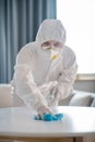 Woman in white workwear and protective gloves looking concentrated while disinfecting the table surface