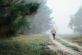 Woman in wide-brimmed felt hat and authentic poncho going along the forest at foggy morning
