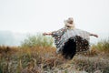 Woman in wide-brimmed felt hat and authentic poncho standing in high brown grass at foggy morning Royalty Free Stock Photo