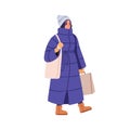 Woman in winter apparel, long puffer coat, hat. Modern girl walking with tote and shopping bags. Female in warm outfit