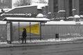 Woman in winter clothes walking alone on a snowy road near bus stop in a little town. Wintertime. Selective focus