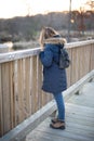 Woman in winter coat looking over railing of bridge at sunset Royalty Free Stock Photo