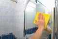 Woman wipes a bathroom mirror with a yellow napkin, concept of cleaning the house