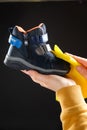 A woman wipes a childs shoe on a black background with a yellow rag. Cleaning from dust and caring for children