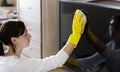 Woman wipes white dust with a TV display in yellow gloves