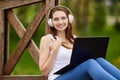 Woman in wireless headphones has telework with laptop outdoors.