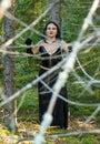 A woman is a witch in black in chains between trees in a dense forest. Halloween.