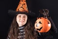A woman in a witch costume in a hat and gloves on a black background holds bucket pumpkin with candy and smile