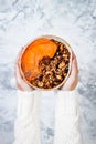 Woman in woolen sweater holding bowl with cinnamon granola, coconut yogurt, chia seeds and pumpkin puree. Healthy vegan smoothie Royalty Free Stock Photo