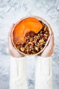 Woman in woolen sweater holding bowl with cinnamon granola, coconut yogurt, chia seeds and pumpkin puree. Healthy vegan smoothie Royalty Free Stock Photo