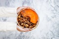 Woman in woolen sweater holding bowl with cinnamon granola, coconut yogurt, chia seeds and pumpkin puree. Healthy vegan smoothie Royalty Free Stock Photo