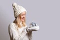 Woman in woolen white sweater, cap with bubo and mittens smiles and looks at Christmas tree toy disco ball