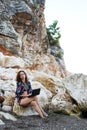 Woman workaholic working on a laptop while sitting on a stone on the beach