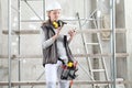 Woman worker builder work with digital tablet, wearing helmet, hearing protection headphones and bag tools, on scaffolding Royalty Free Stock Photo