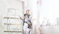 Woman worker builder work with digital tablet, wearing helmet, hearing protection headphones and bag tools, on scaffolding