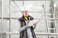 Woman worker builder work with digital tablet, wearing helmet and hearing protection headphones , on scaffolding construction site Royalty Free Stock Photo