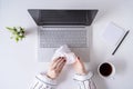 A woman worker cleaning with antivirus wet wipe a laptop and a working office desk before starting work for protect herself