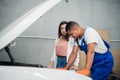 Woman and worker inspect broken car engine