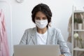 Woman in medical mask working on laptop in office