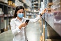 Woman worker with medical mask using smartphone to checking inventory in warehouse during coronavirus covid-19 pandemic Royalty Free Stock Photo
