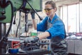 Woman worker in metal workshop greasing drill