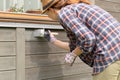 Woman worker painting wooden house exterior wall with paintbrush and wood protective color