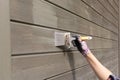 Woman worker painting wooden house exterior wall with paintbrush and wood protective color