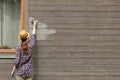 Woman worker painting wooden house exterior wall with paintbrush and wood protective color