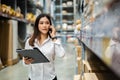 Woman worker talking on a mobile phone and holding clipboard to checking inventory in the warehouse store Royalty Free Stock Photo