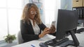 Woman working in a bright office using her smartphone and desktop computer, smiling and wearing glasses Royalty Free Stock Photo