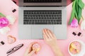 Woman working with computer. Office desk with laptop, tulip flowers, glasses, pen and cookies on pink background. Flat lay. Top vi