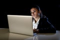 Woman working in darkness on laptop computer late at night looking stressed bored and tired