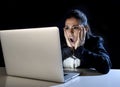 Woman working in darkness on laptop computer late at night surprised in shock and stress Royalty Free Stock Photo